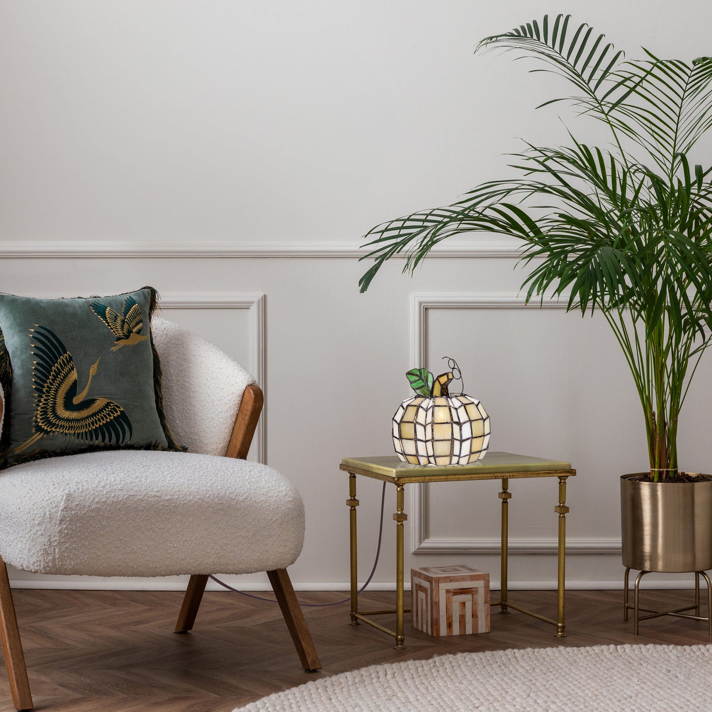 9"H Patch the Pumpkin Stained Glass Accent Lamp sits on a small gold side table in a styled living room corner next to a white boucle armchair and a potted palm.