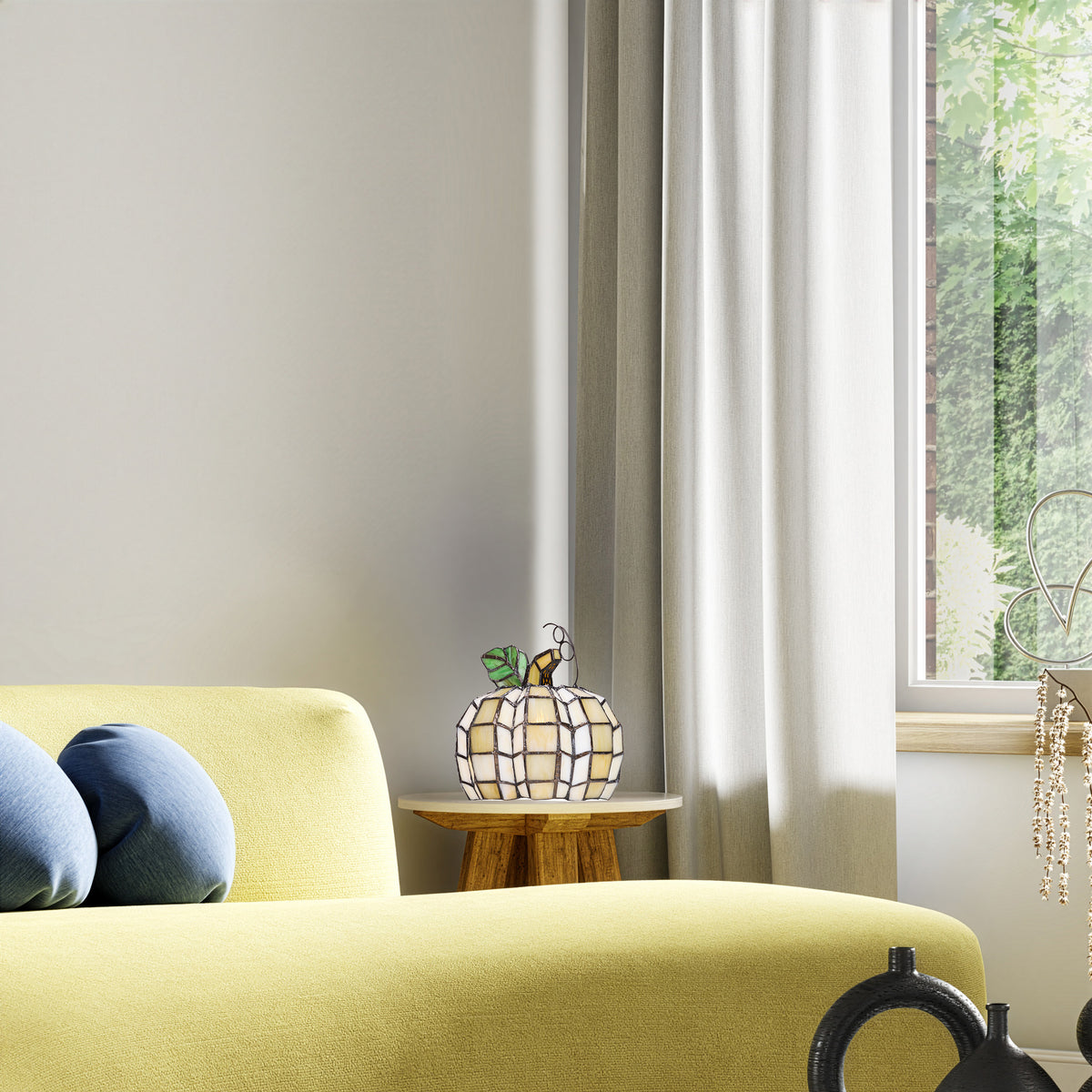 9"H Patch the Pumpkin Stained Glass Accent Lamp in a styled interior corner with a pale yellow-green sofa, blue pillows and a small wooden side table. A tall white curtain hangs beside a window showing greenery outside.